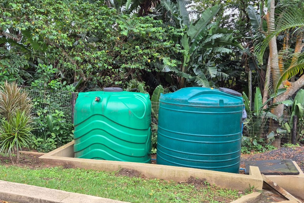 Two green plastic water storage tanks situated on a concrete base within a landscaped garden area.