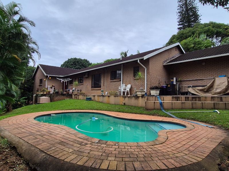 Rear exterior view of the house featuring a swimming pool with brick paving, a brick facade, and a landscaped garden area.