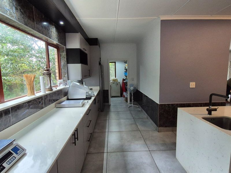 A modern kitchen featuring quartz countertops, sleek cabinetry, tiled flooring, and a functional layout with an adjacent scullery area.