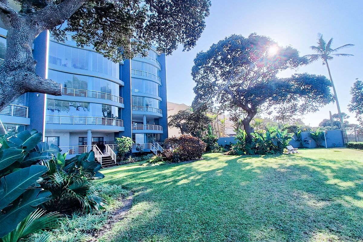 Rear view of the apartment building featuring multi-level enclosed balconies with glass balustrades, set within a well-maintained garden with mature trees.