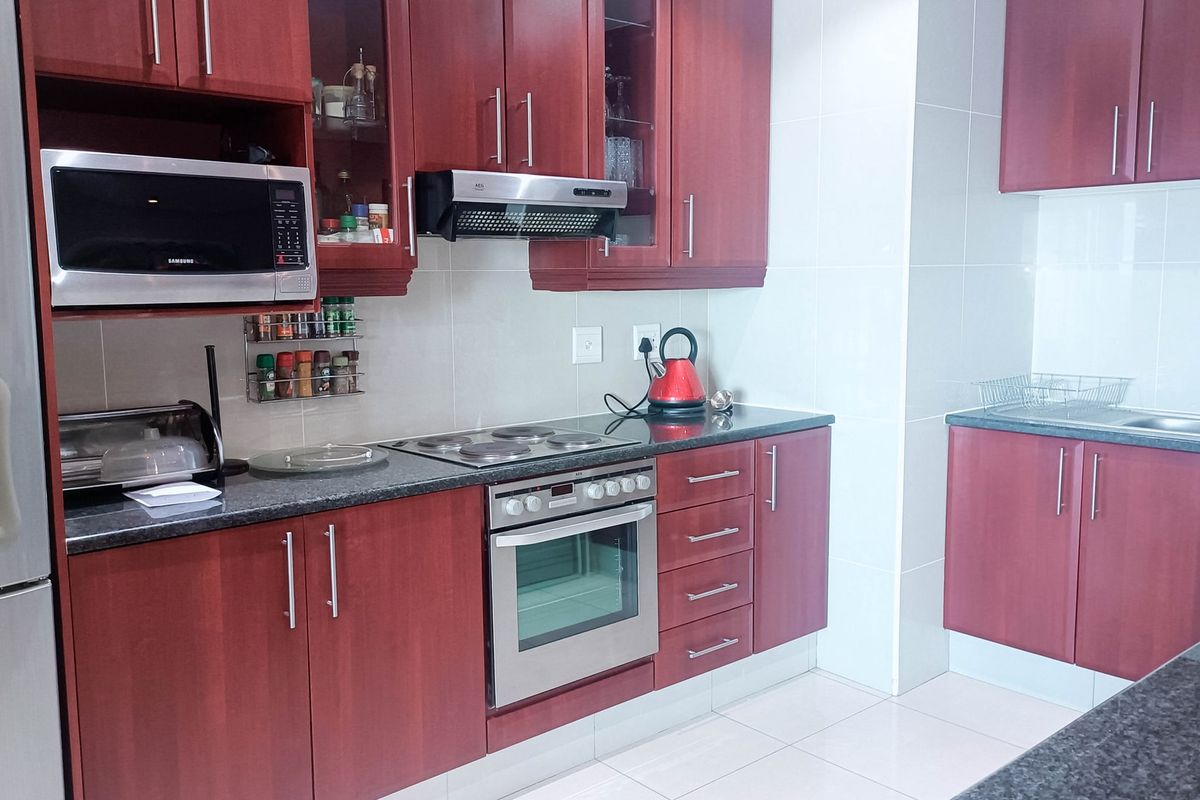 A functional kitchen featuring cherry-wood cabinetry, granite countertops, integrated appliances including an oven and hob, and neutral tiled finishes.