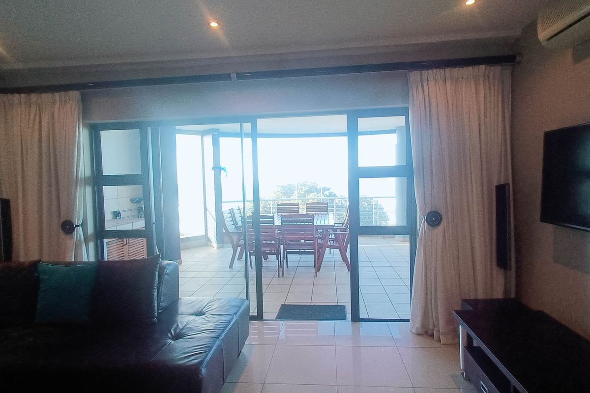 Spacious living area featuring tiled floors, recessed lighting, and large sliding glass doors that open onto a private balcony with outdoor seating.