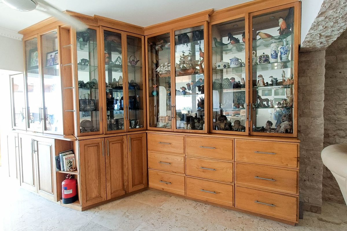 Living area featuring extensive custom built-in wooden cabinetry with glass display shelving and durable stone flooring.