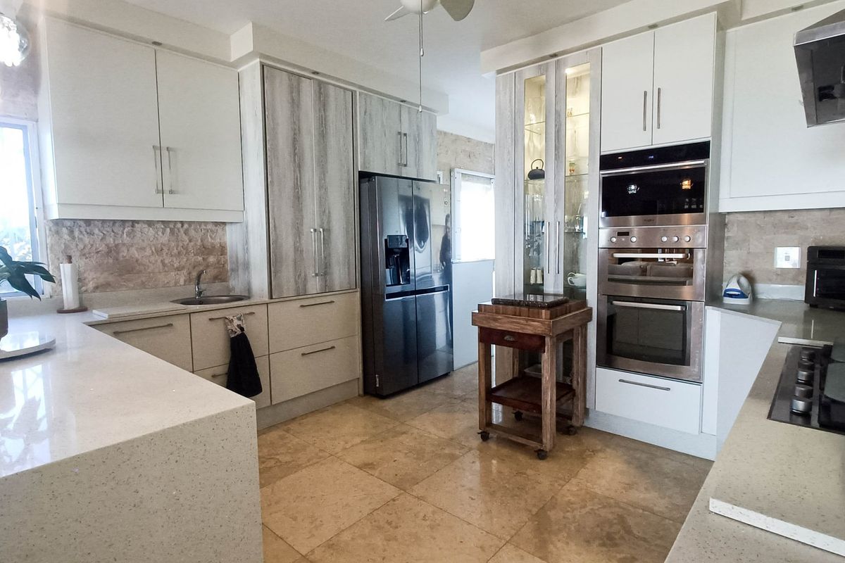 Modern kitchen featuring stone countertops, built-in oven and microwave, stone tile flooring, and a mix of white and wood-grain cabinetry.