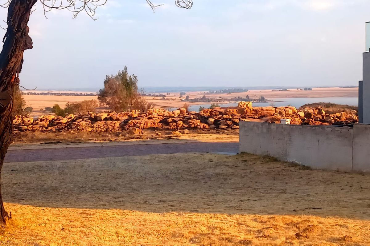 A scenic view overlooking a rocky landscape and distant water, featuring a partial view of a residential retaining wall.