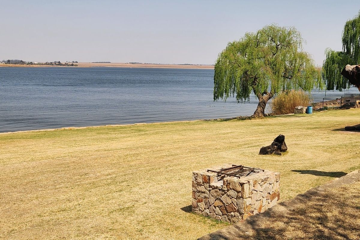A scenic waterfront view featuring a stone-clad braai area set on a spacious lawn overlooking the dam.