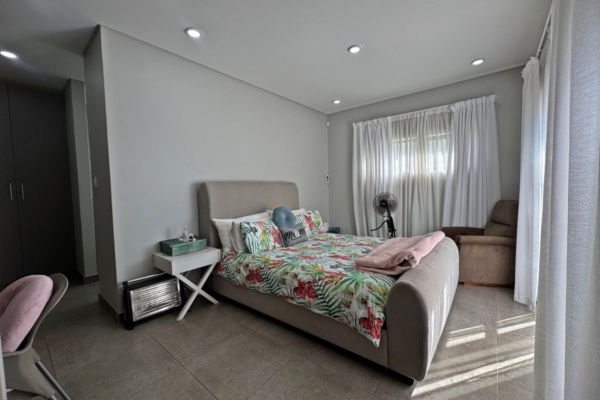 A spacious bedroom featuring neutral tiled flooring, recessed downlighting, and built-in storage cupboards, offering a clean and functional living space.