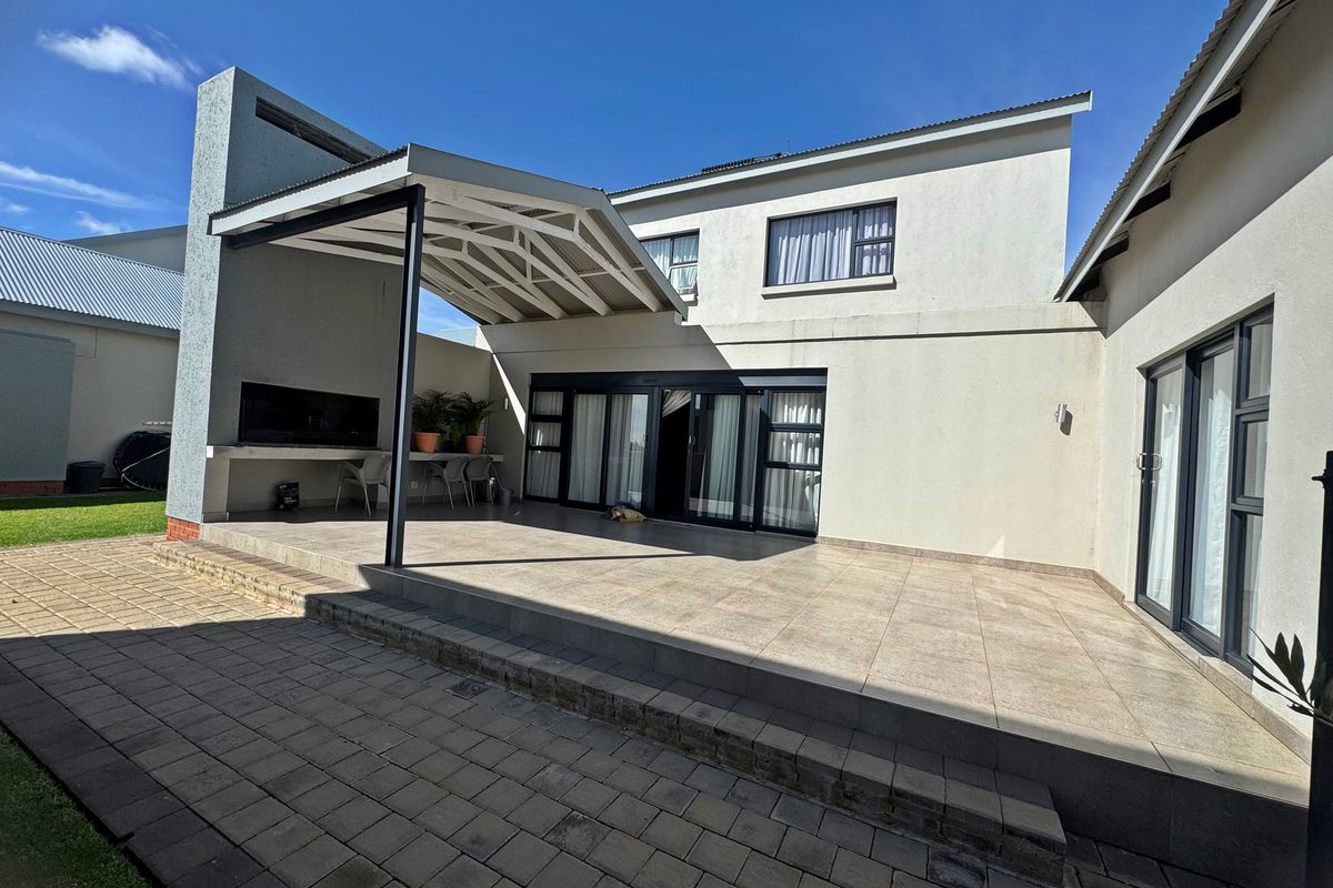 Spacious rear exterior featuring a covered patio with a built-in braai, tiled flooring, and large sliding doors leading into the home.