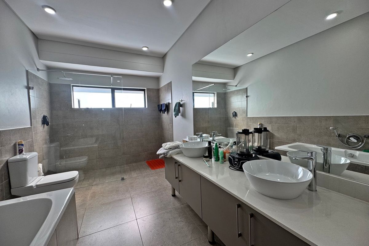 Modern bathroom featuring a double vanity with vessel sinks, a spacious walk-in shower with glass screen, a built-in bathtub, and contemporary tiled finishes.