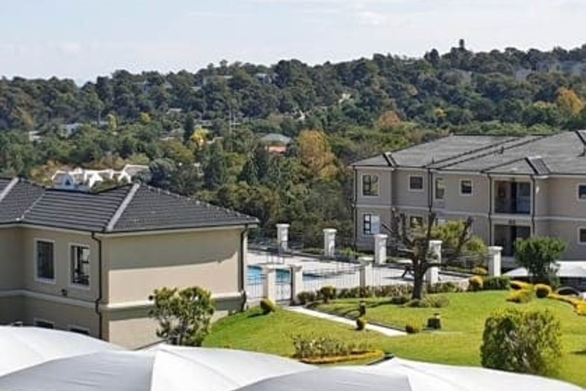 An elevated aerial view of the apartment complex, showcasing the building architecture, communal swimming pool, and well-maintained landscaped garden areas.