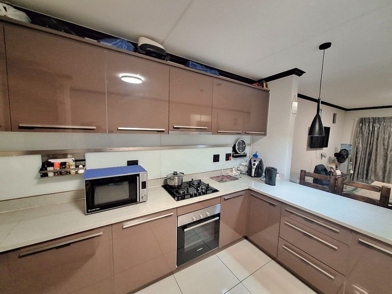 Modern kitchen featuring high-gloss cabinetry, stone countertops, a gas hob, and a built-in oven, seamlessly integrated into an open-plan living space.