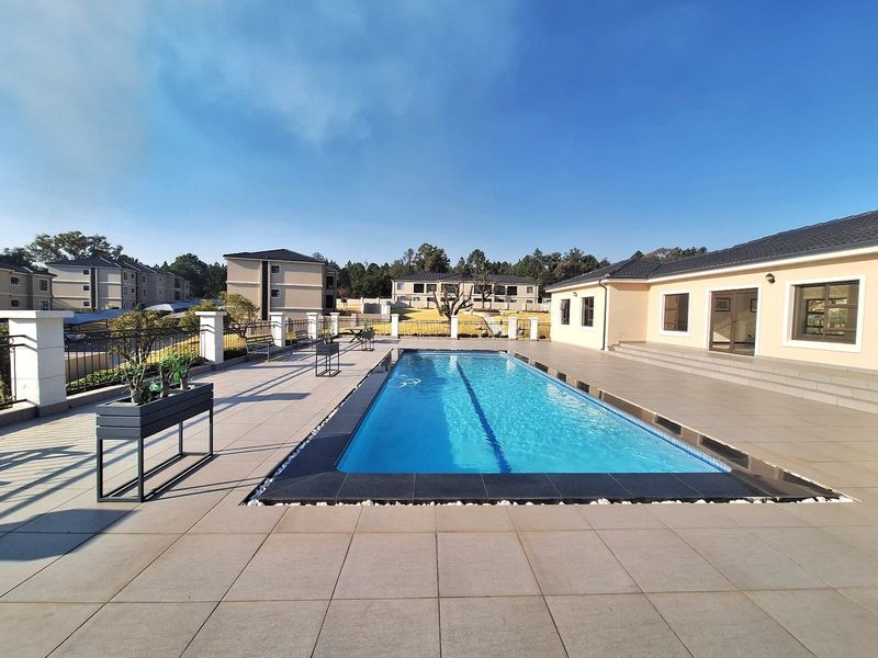 A well-maintained communal swimming pool area featuring a tiled deck, clear water, and surrounding perimeter fencing within a residential apartment complex.