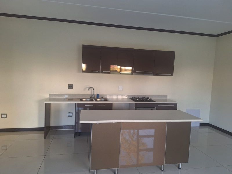 Modern kitchen featuring sleek brown cabinetry, stone countertops, a central island, and integrated gas hob and oven, set against neutral tiled flooring.