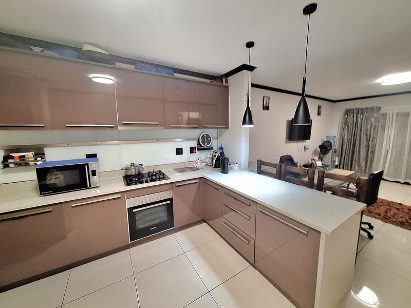 Open-plan kitchen featuring modern high-gloss cabinetry, stone countertops, built-in oven, and gas hob, seamlessly flowing into the adjacent living and dining area.