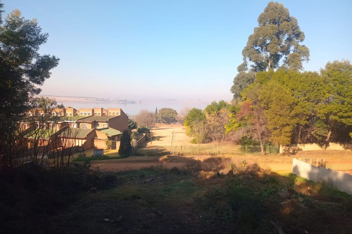 A scenic view overlooking a vacant residential plot with mature trees, perimeter fencing, and distant water views.
