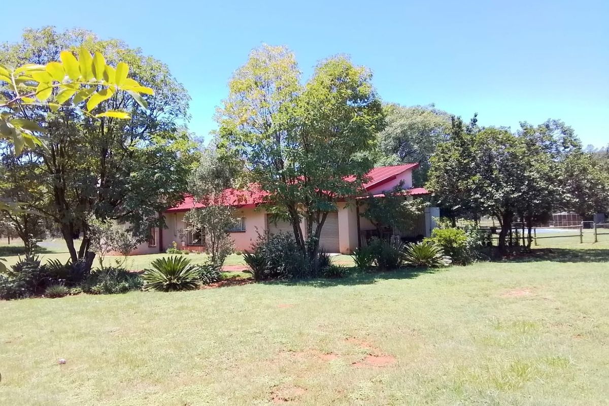 A view of the rear elevation of the house featuring a red metal roof, garage access, and established garden surroundings.
