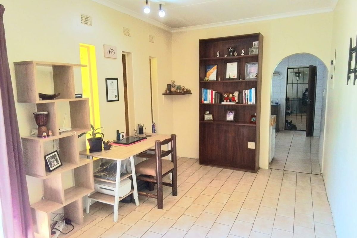 A living area featuring ceramic floor tiles, a built-in wooden shelving unit, and an arched doorway leading to an adjacent space.