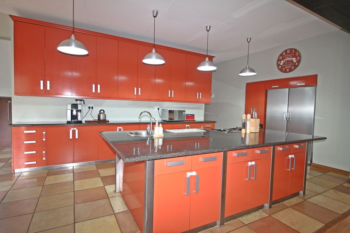 Spacious kitchen featuring vibrant orange cabinetry, a large central island with granite countertops, stainless steel sink, and modern pendant lighting over the workspace.