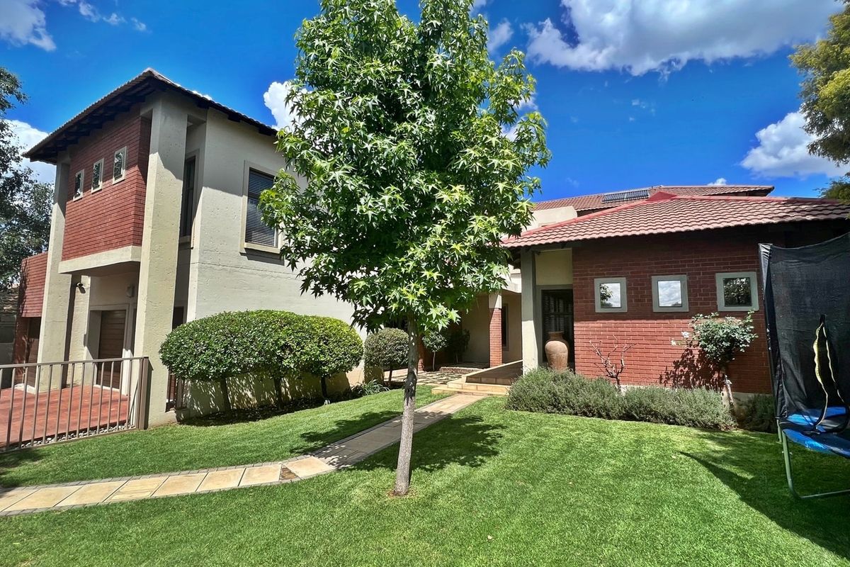 A well-maintained rear garden featuring a paved walkway, established lawn, and a multi-level brick and plaster facade with a tiled roof.