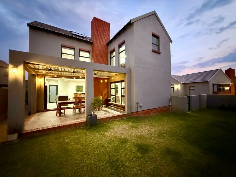 Rear view of a two-story townhouse featuring a covered patio, exposed brick chimney, and a well-maintained lawn at dusk.
