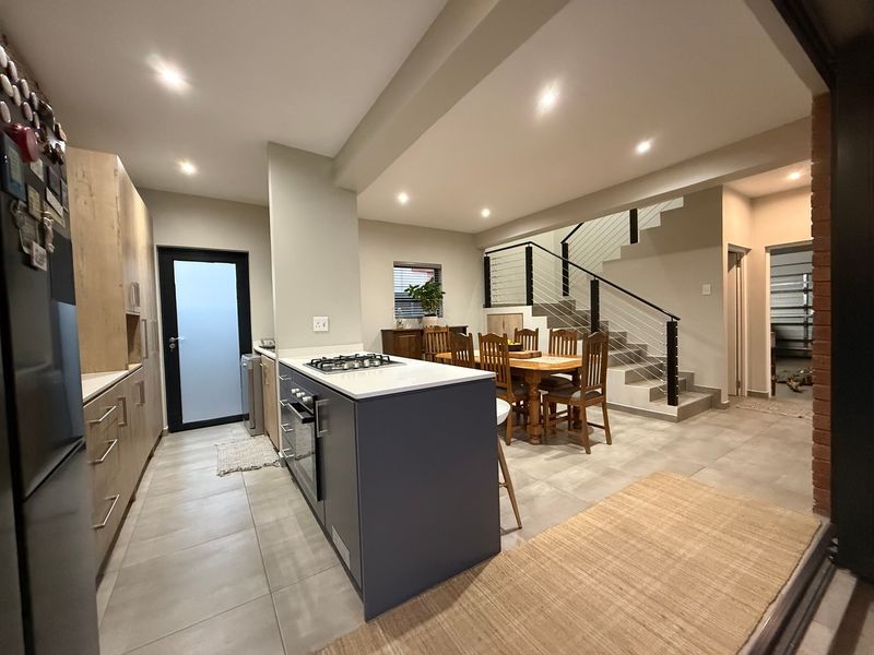 Open-plan kitchen and dining area featuring a central island with gas hob, modern cabinetry, tiled floors, and a staircase with a contemporary metal balustrade.