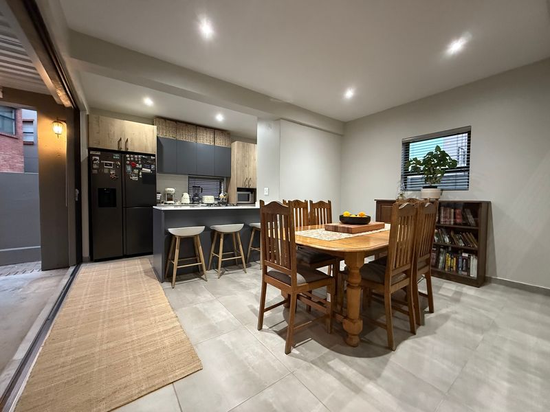 An open-plan kitchen and dining area featuring modern cabinetry, a central island, recessed lighting, and large format floor tiles with direct access to the outdoors.