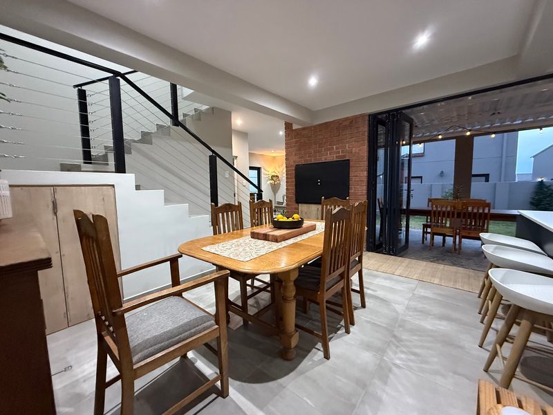 Open-plan living and dining area featuring a modern staircase with metal balustrade, exposed brick wall, and bi-fold doors leading to an outdoor patio.