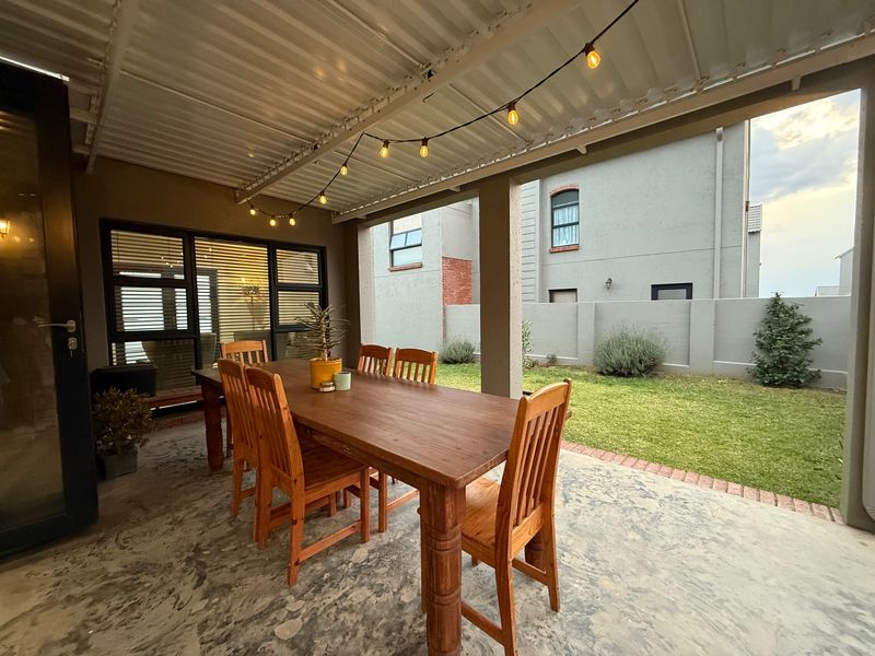 A covered outdoor patio area featuring a concrete floor, corrugated metal roof, and direct access to a private garden space.