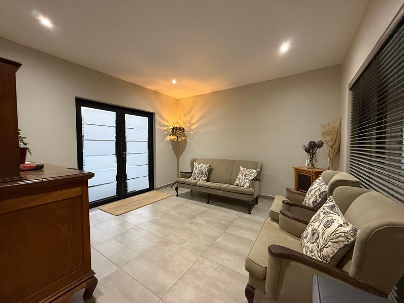 A well-maintained living room featuring large format floor tiles, recessed lighting, and modern frosted glass double doors leading to an outdoor area.
