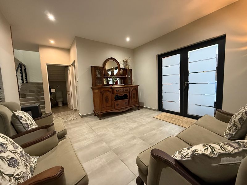 A well-maintained living area featuring large format floor tiles, recessed lighting, and double glass doors leading to the exterior, with an adjacent staircase.