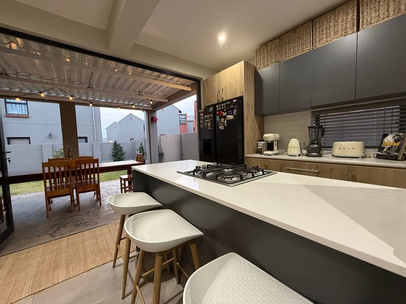Modern open-plan kitchen featuring a central island with gas hob, sleek cabinetry, and seamless flow to a covered outdoor patio area.