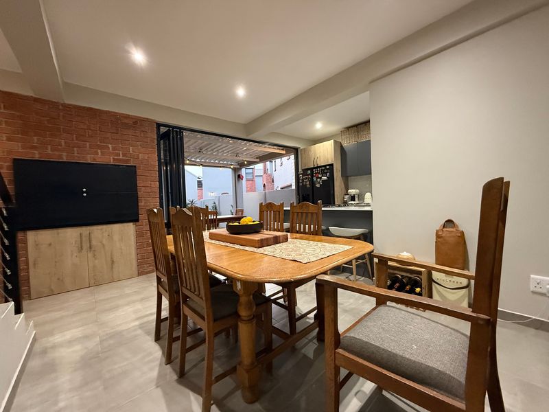 Open-plan dining and kitchen area featuring an exposed brick wall, modern tiled flooring, and seamless indoor-outdoor flow through bi-fold doors to the patio.