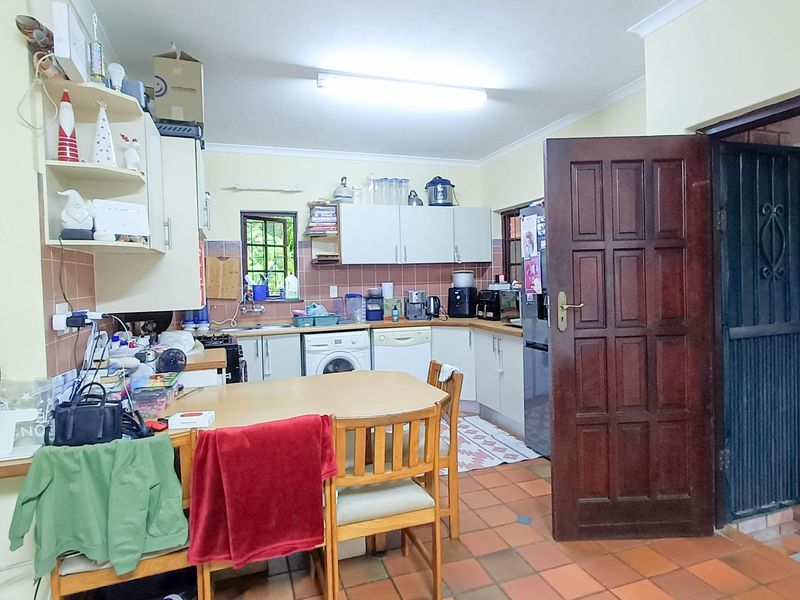 A functional kitchen featuring built-in cabinetry, tiled backsplash, and tiled flooring, with direct access to an adjacent area.