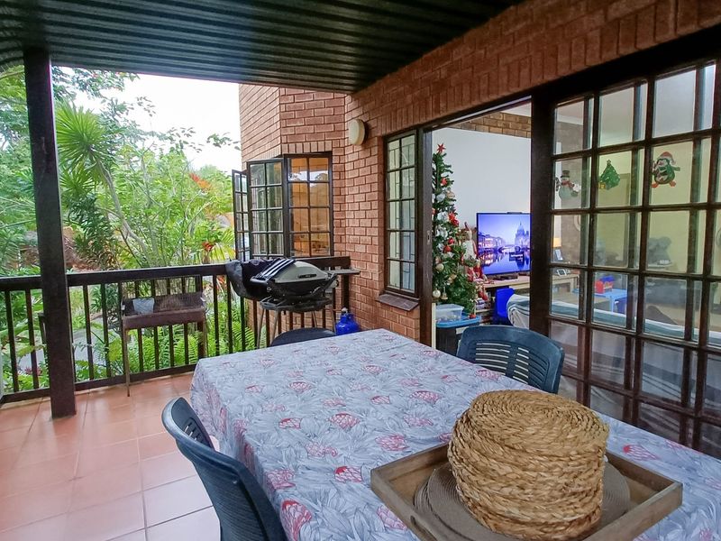 A covered outdoor patio featuring tiled flooring, brick walls, and a timber balustrade, providing direct access to the interior living space through sliding glass doors.