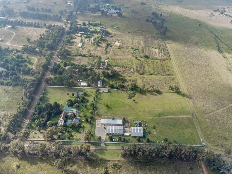 An aerial view of the farm property, showcasing the main residence, swimming pool, outbuildings, and expansive surrounding land.