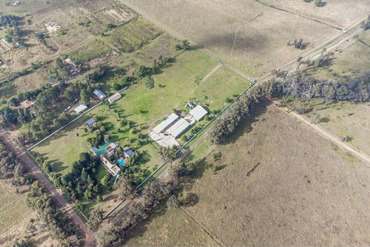 Aerial view of a farm property featuring a main residence, swimming pool, multiple outbuildings, and expansive surrounding land.