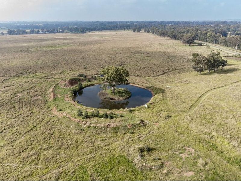 An aerial view of a farm property featuring a circular dam with a central island and mature tree, surrounded by expansive open grazing land.
