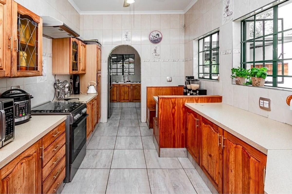 A functional kitchen featuring extensive wooden cabinetry, tiled splashbacks, and a tiled floor, with an arched opening leading to an adjacent scullery area.
