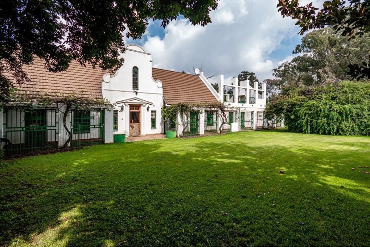 Rear view of a Cape Dutch style farmhouse featuring a large lawn, tiled roof, and secure metal gated entrances along the building facade.