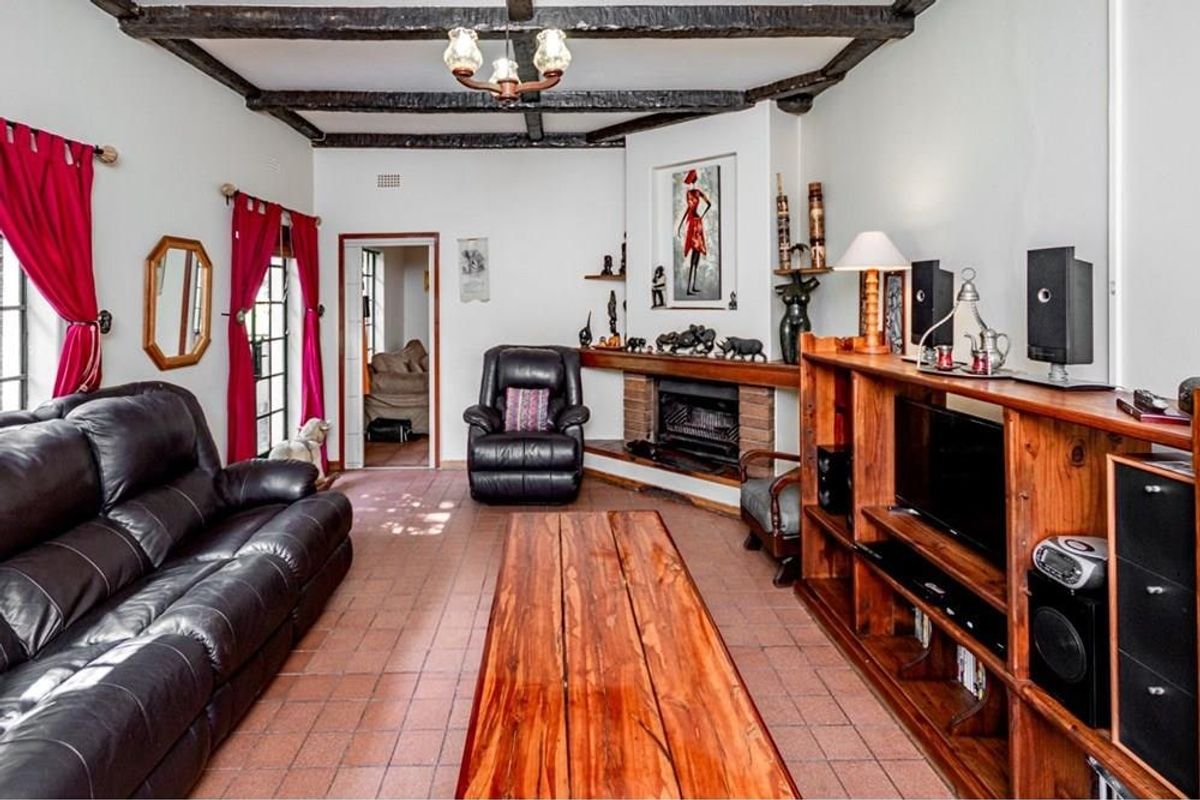 A cozy living room featuring exposed timber ceiling beams, a corner brick fireplace, and durable tiled flooring, creating a rustic and inviting atmosphere.