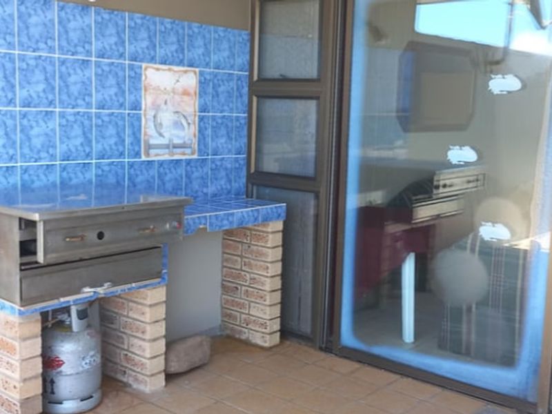 Covered patio area featuring a built-in braai with tiled splashback and brick base, providing direct access to the interior living space via sliding doors.
