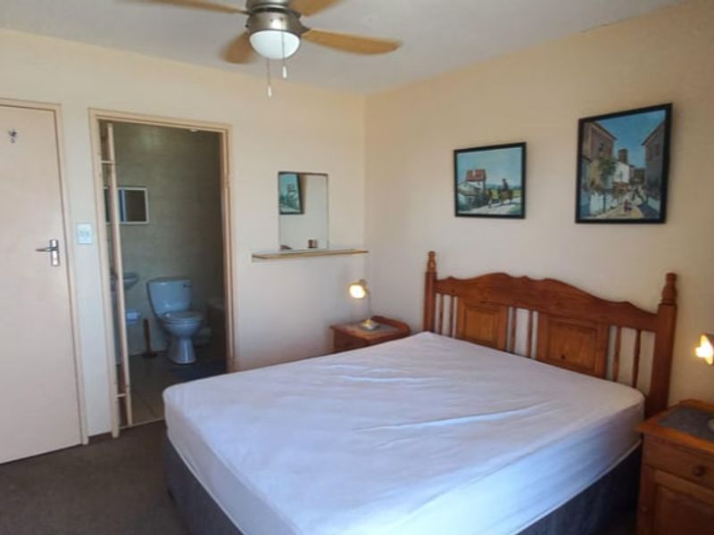 A bedroom featuring a ceiling fan and an attached en-suite bathroom with standard finishes.
