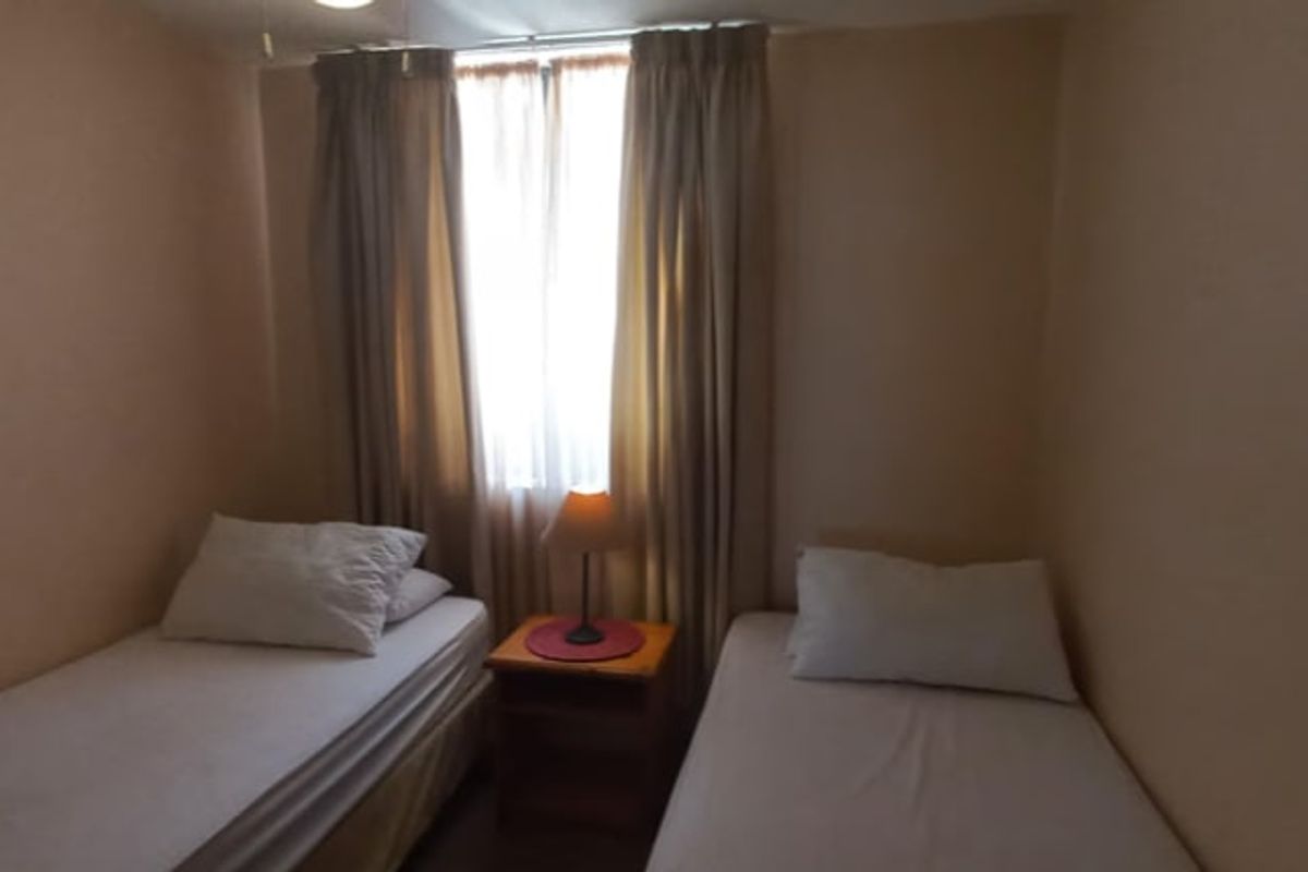A compact bedroom featuring a window with curtains, providing natural light and space for two single beds.