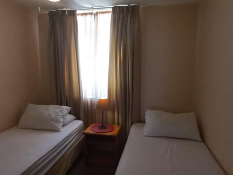 A compact bedroom featuring a window with curtains, providing natural light and space for two single beds.
