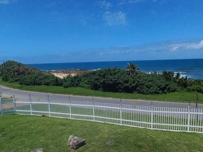 A scenic coastal view overlooking a road, lush greenery, and the ocean, secured by a white picket fence with integrated electric fencing.