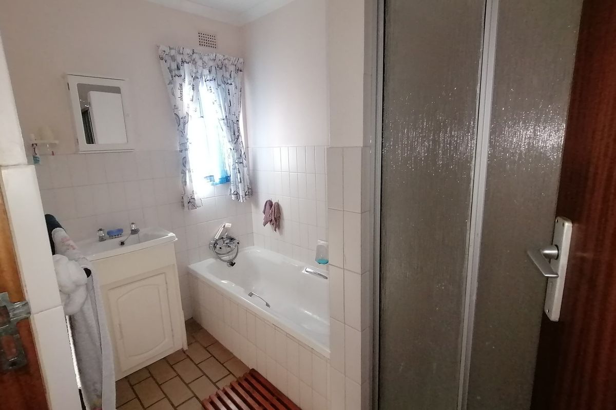 A functional bathroom featuring a bathtub, separate shower enclosure, and vanity basin with wall-to-wall tiling.
