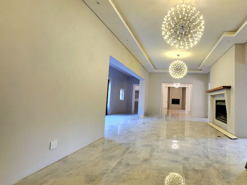 Spacious open-plan living area featuring polished marble flooring, recessed tray ceilings with modern pendant lighting, and a built-in fireplace with a wooden mantel.