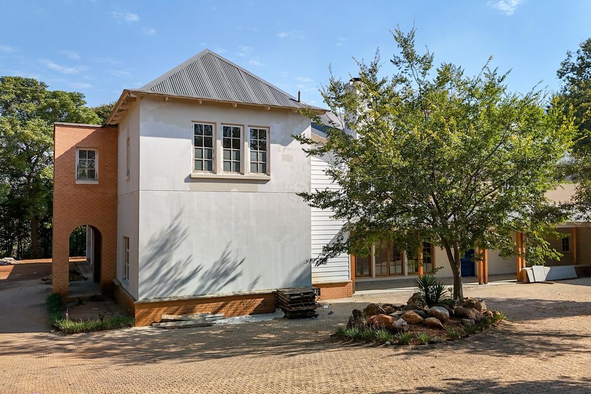 A view of the rear exterior of the house featuring a mix of brick and plastered walls, a corrugated metal roof, and a paved courtyard area.