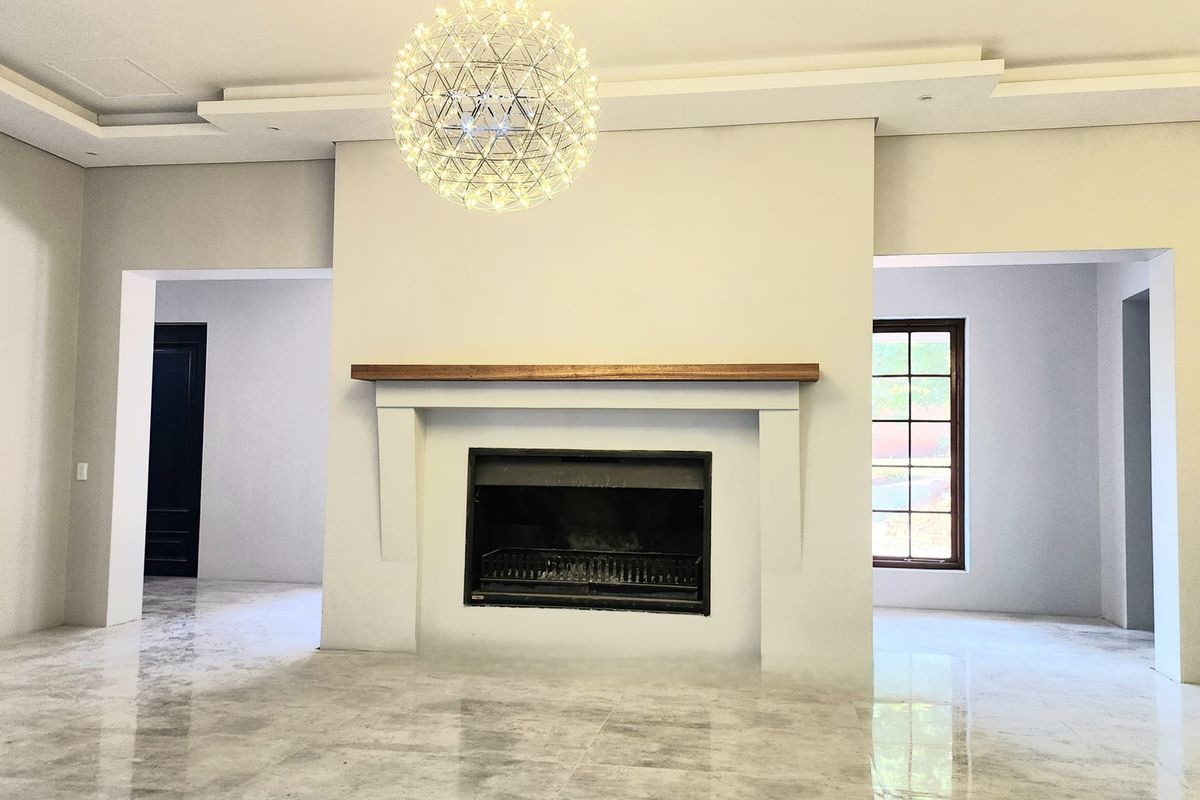 Spacious living area featuring a central built-in fireplace with a wooden mantel, polished marble-style flooring, and recessed ceiling detail with a modern pendant light.