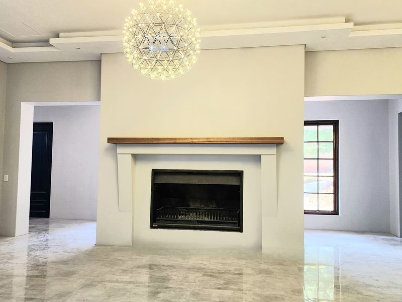 Spacious living area featuring a central built-in fireplace with a wooden mantel, polished marble-style flooring, and recessed ceiling detail with a modern pendant light.